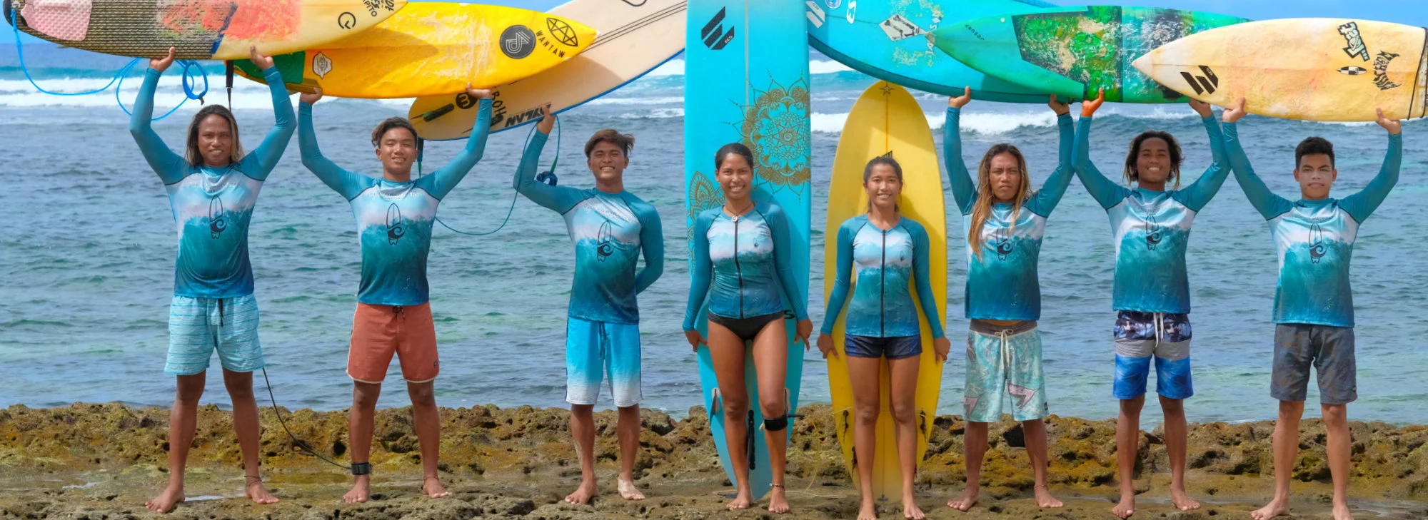 Surfing team in customized blue rash guards holding surfboards beside the sea